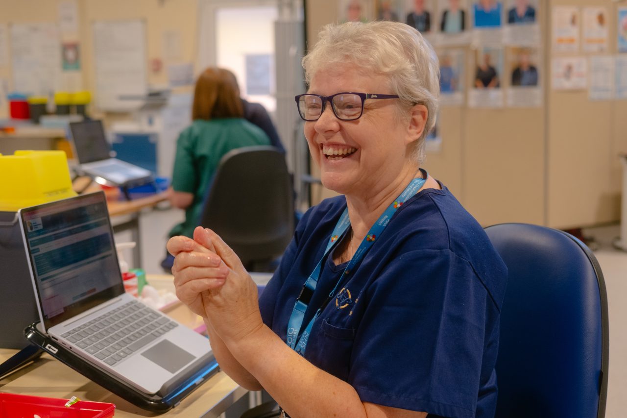 Aelod staff Bwrdd Iechyd Addysgu Powys mewn sefydliad clinigol gyda gliniadur.