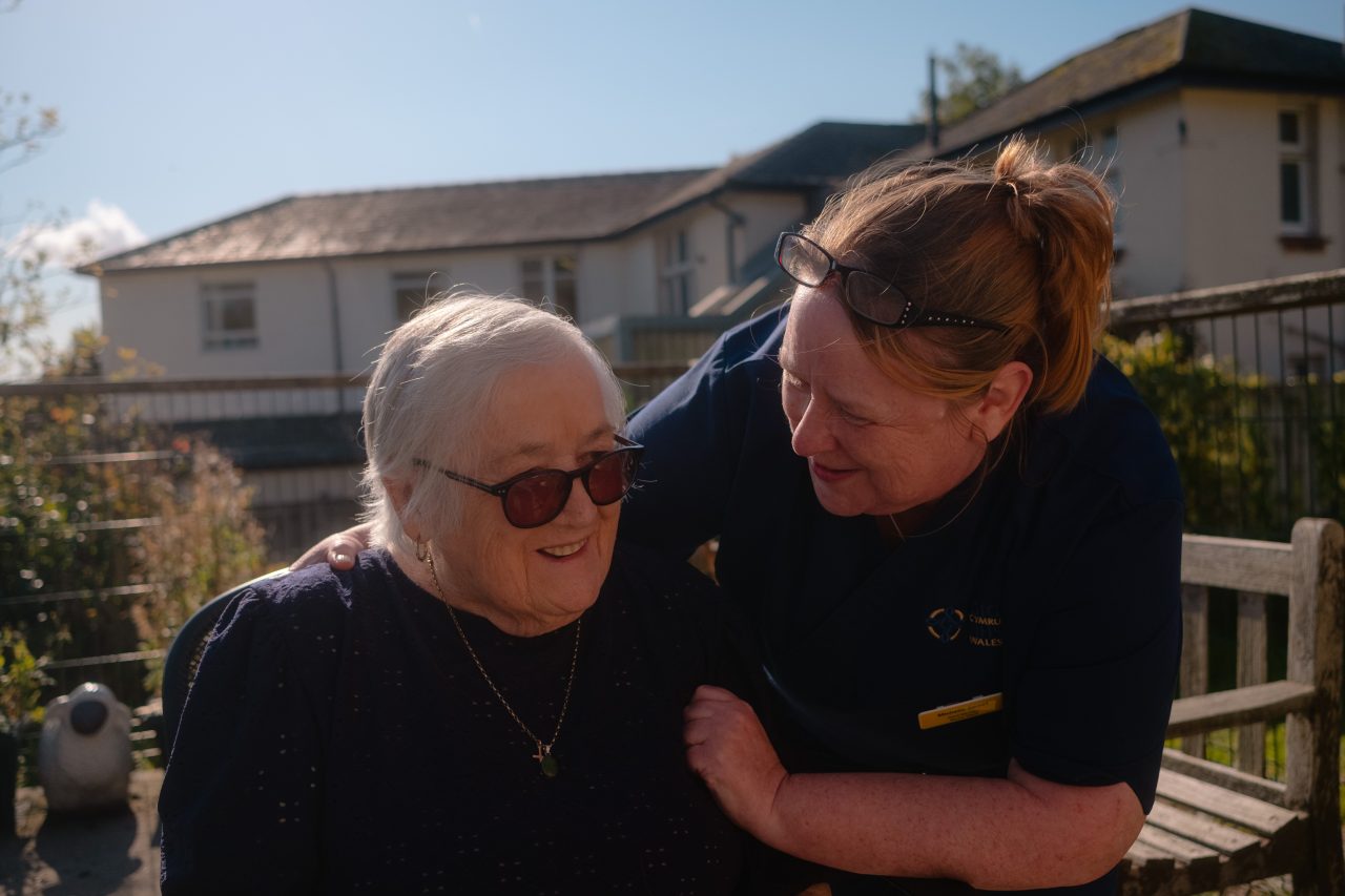 Aelod o staff Bwrdd Iechyd Addysg Powys gyda braich o amgylch claf.
